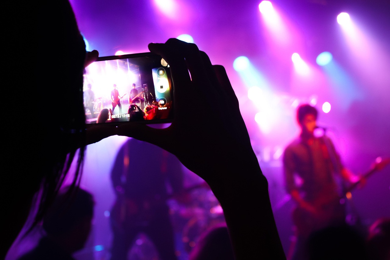 Fan filming the band on a phone under stage lights